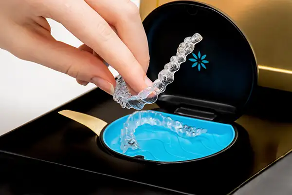 Close-up of a hand pick up an Invisalign clear aligner from its sleek packaging, showing off the thin, light material used for upper teeth.